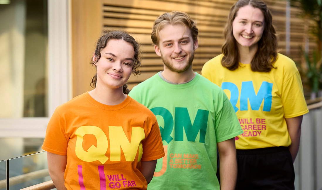 Three smiling students wearing colourful QMU promotional t-shirts.